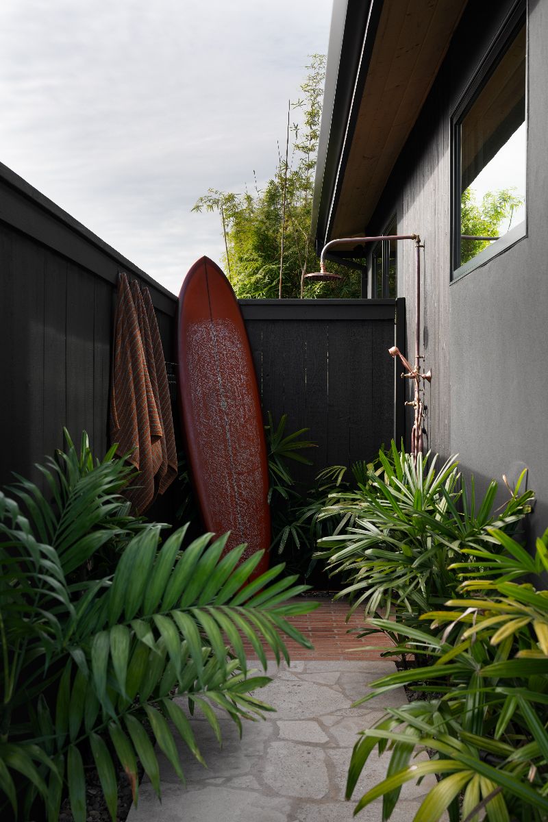 Private area with outside shower next to surf board and ferns
